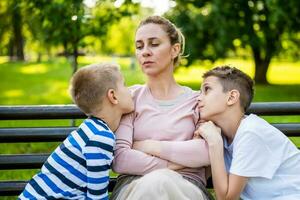 madre es sentado con su hijos en banco en parque. ella es enojado y el Niños tratar a disculparse. foto