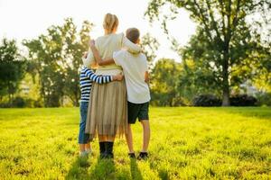 contento madre es abrazando con su hijos en parque. ellos son abrazando y disfrutando puesta de sol. foto