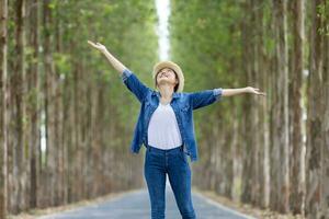 Asian tourist woman is jumping and dancing while having vacation at the national park while walking on the road with column of tree for travel and adventure photo