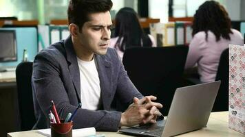 Video of young male  employee showing serious expression while typing on his laptop