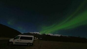 Skaftafell, Iceland, 2023 - Campervan stand on parking in Skaftafell campground with couple watch Aurora northern lights at night over snowy mountain peak in Skaftafell, Iceland video