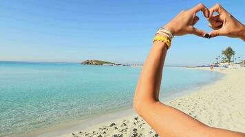 contento niña turista en soleado nisi playa en Chipre espectáculo dedo conformado corazón forma signo. manos de niña forma de corazón. verano sueño. felicidad de libertad en Días festivos vacaciones video