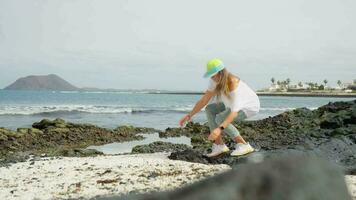 A girl in white on a volcanic beach touches pebbles. video