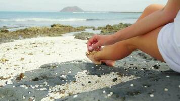 A girl in white sits against of the sea and touches small pebbles on the shore. video