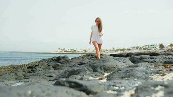 il ragazza passeggiate su il pietre nel un' bianca maglietta, abbronzato gambe. video