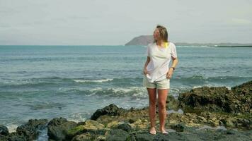 Mädchen im ein Weiß T-Shirt auf das Strand, im das Entfernung Sie können sehen das Insel video