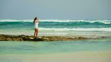 A girl in white stands on a narrow strip of rock. Fuerteventura video