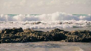 Sea waves crash against the coastal rocks on the sandy beach. video