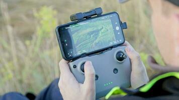 drone operator hands using remote control with sticks and cellphone as monitor at daylight video