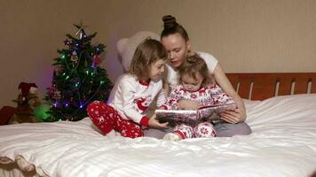 Young mother between 30 and 35 years old reads fairy tales to her small children in the bed. Winter holidays period. video