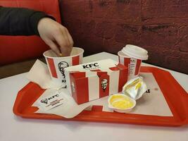 Stavropol, RUSSIA - April 2023 KFC fast food restaurant. Man taking out french fries from a box photo