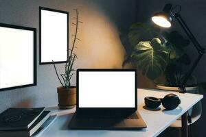 Notebook computer, leave blank, white mockup and black frame, leave blank for use. There are lamps and books on the desk, decorated with plants and leaves planted in the house. photo