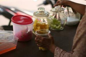 indonesio calle vendedor manos preparar un vaso de borde del camino Fruta hielo como clientes pacientemente Espere para su pedidos. foto