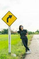 Woman stand with backpack hitchhiking along a road photo