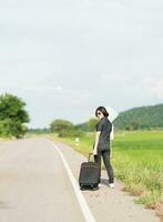 Woman with luggage hitchhiking along a road photo