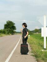 Woman with luggage hitchhiking along a road photo