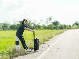 Woman with luggage hitchhiking along a road photo