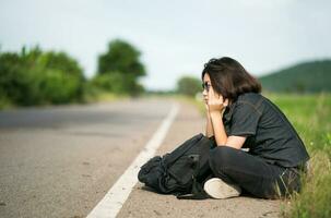 Woman sit with backpack hitchhiking along a road in countryside photo