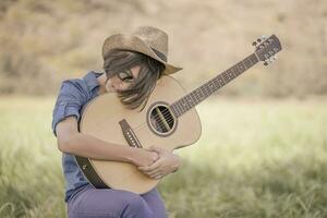 Women short hair wear hat and sunglasses sit playing guitar in grass field photo