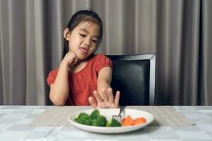 Little cute kid girl refusing to eat healthy vegetables. Children do not like to eat vegetables. photo