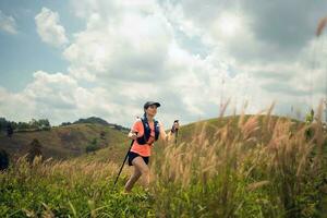 Young women active trail running across a meadow on a grassy trail high in the mountains in the afternoon with trekking pole photo