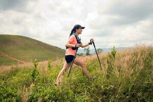 sendero activo para mujeres jóvenes que atraviesa un prado en un sendero cubierto de hierba en lo alto de las montañas por la tarde con bastón de trekking foto