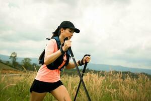 sendero activo para mujeres jóvenes que atraviesa un prado en un sendero cubierto de hierba en lo alto de las montañas por la tarde con bastón de trekking foto