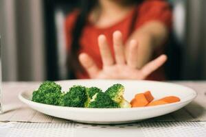 Little cute kid girl refusing to eat healthy vegetables. Children do not like to eat vegetables. photo