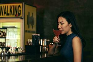 Asian woman drinking a cocktail at a bar at night. photo