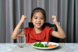 Kid shows strength of eats vegetables and nutritious food. photo