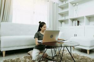 Young asian woman sits in the living room using a calculator to calculate family income and expenses and writes it down in his notebook or laptop at home. photo