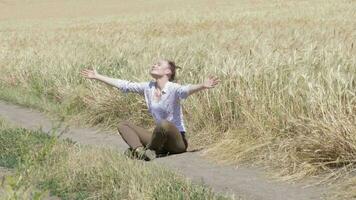 Young lady sitting in the middle of the road on the wheat field video