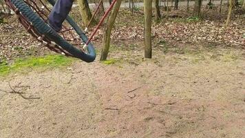 Child in outdoor action on forest playground swing in slow motion has fun while swinging on rainy day in the forest with happiness and joyful recreation as outdoor adventures in close-up and shoes video