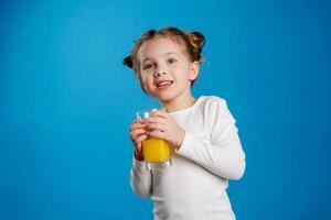 retrato de un pequeño niña de eslavo apariencia Bebiendo naranja jugo en un azul antecedentes foto