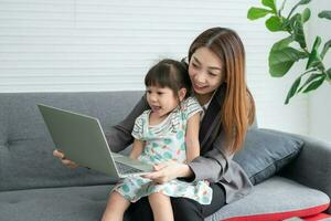 Asian mother with her two grandchildren having fun and playing education games online with a digital computer laptop at home in the living room. Concept of online education and caring from parents. photo