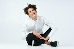 guy with curly hair in a white shirt, sneakers and trousers sits on the floor photo