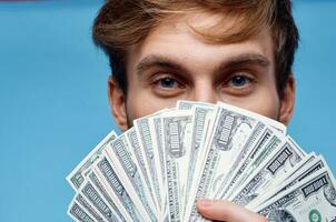 a man with a wad of money covers his face close-up blue background photo