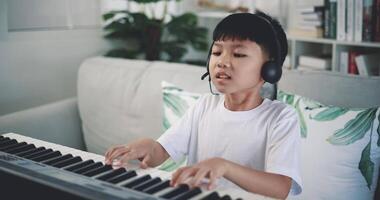 handhållen skott, kreativ asiatisk pojke bär hörlurar med konstnärlig Kompetens tar musik lektioner uppkopplad under en video ring upp och spelar de piano på Hem. musik, hobby och livsstil begrepp.