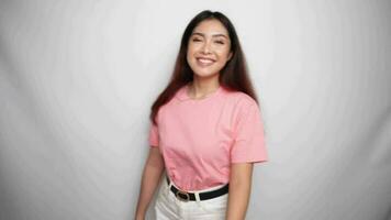 sonriente joven asiático mujer es vistiendo rosado camisa, gesticulando tradicional saludo en estudio con blanco antecedentes video