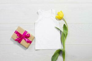 White children t-shirt mockup. Template blank kids shirt top view. White wooden background. Mother women day holiday. Yellow tulip. Baby tshirt with birthday flower. Spring look. photo