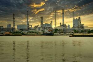 un petróleo refinería situado en el chao phraya río, en bangkok, tailandia, un grande industrial fábrica. y el dorado noche cielo grande nubes cuando es acerca de a lluvia foto