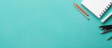 A notebook, pencils, and a pair of scissors on a turquoise background created with technology photo