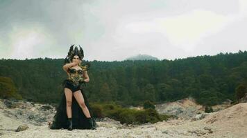 a witch in a black dress and crown posing with a scary expression in a mountain video