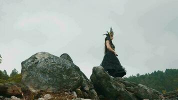 un bruja en un negro vestido y corona bailes en un rock en un montaña video