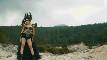 a witch in a black dress and crown posing with a scary expression in a mountain video