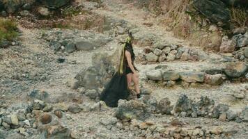 a gothic woman in a black dress walking in a mountain crater filled with rocks video