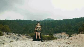 a gothic woman in a black costume walks in the middle of a crater full of rocks video