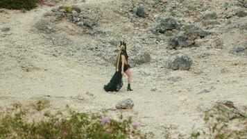 a gothic woman in a black dress walking in a mountain crater filled with rocks video