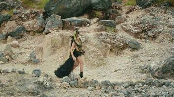 a gothic woman in a black dress walking in a mountain crater filled with rocks video