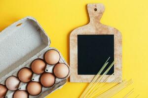 raw eggs in a package with pasta next to a cutting board with empty space for your text photo